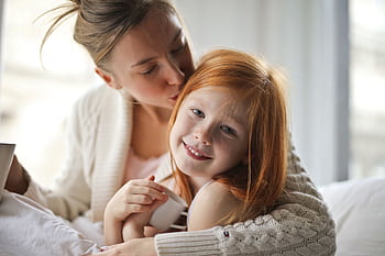 A mother tenderly hugging her smiling daughter indoors, showcasing love and warmth. HD wallpaper