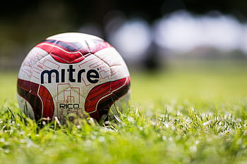 A close-up of a Mitre soccer ball resting on a grassy field with a blurred background. HD wallpaper