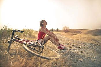 A woman enjoying a serene moment with her bicycle on a country road at sunset, embracing nature and tranquility. HD wallpaper