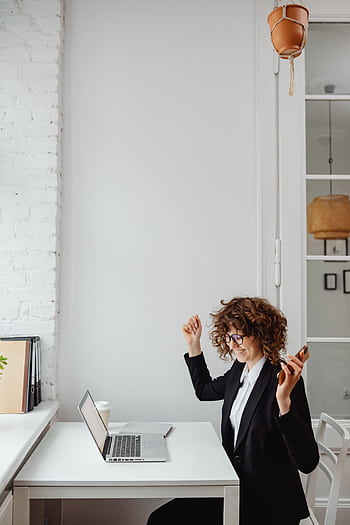 Businesswoman with curly hair celebrates success on call in modern office with laptop. HD phone wallpaper