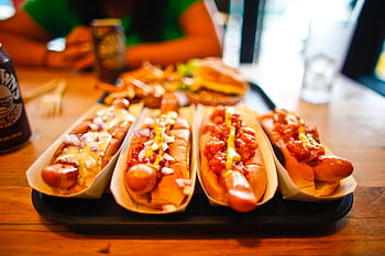 Close-up of various hotdogs with toppings on a wooden table, ideal for fast food themes. HD wallpaper