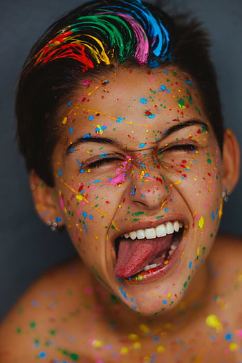Person enjoying a burst of creativity with colorful paint on face, showing excitement. HD phone wallpaper
