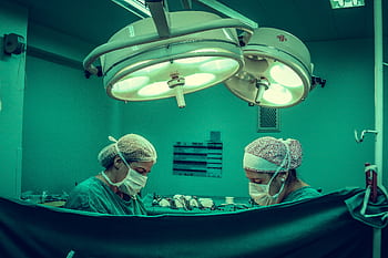 Surgeons in an operating room conducting a medical procedure under bright surgical lights. HD wallpaper