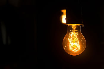 Close-up view of an illuminated vintage light bulb with glowing filament against a dark background. HD wallpaper