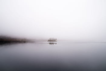 A tranquil misty lake scene with an island reflecting in the calm waters on a foggy day. HD wallpaper