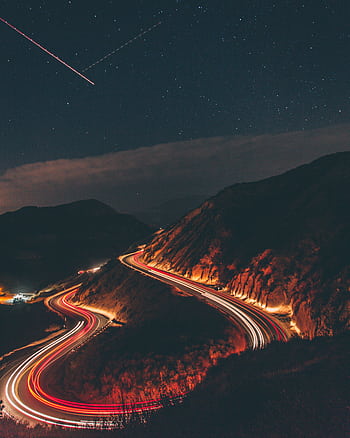 A captivating long exposure shot of a winding highway at night with car light trails under a starry sky. HD phone wallpaper