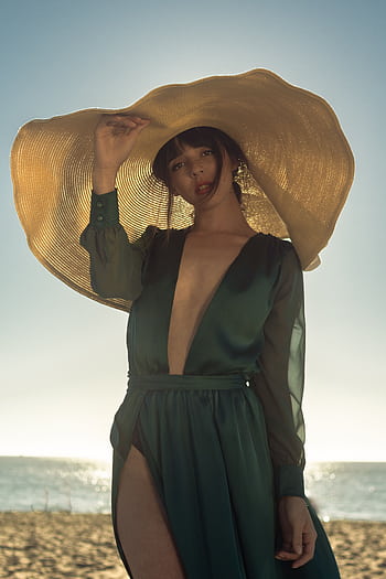 Elegant woman in green dress and sun hat posing on a sunny beach. HD phone wallpaper