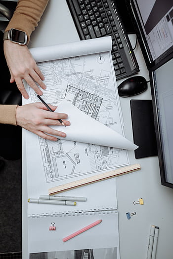 High-angle view of an architect reviewing construction drawings on a desk in an office. HD phone wallpaper