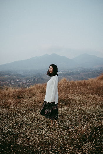 Woman standing in a serene meadow, Bandung, Indonesia, with mountains in the background. HD phone wallpaper