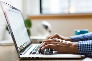 Close-up of adult typing on laptop in bright, modern office. HD wallpaper