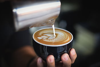 Close-up of a barista pouring milk to create latte art in a coffee cup. HD wallpaper