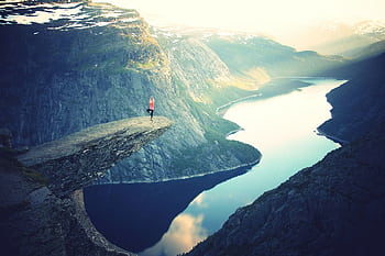 A person meditates in a serene yoga pose on a cliff overlooking breathtaking fjords. HD wallpaper