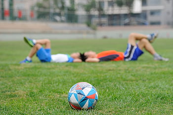 Two teenagers lying on grass near a soccer ball, enjoying leisure time outdoors. HD wallpaper