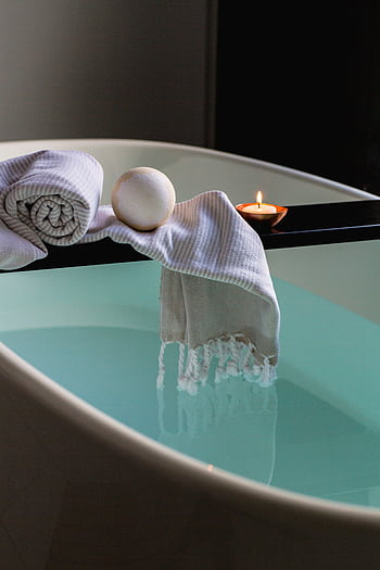 Elegant indoor spa setting with bathtub, candle, towel, and bath bomb for relaxation. HD phone wallpaper
