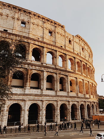 Iconic view of the Colosseum in Rome, Italy, at sunset with tourists outside. HD phone wallpaper