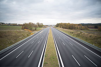 A serene of an empty highway stretching through a peaceful countryside under a cloudy sky. HD wallpaper