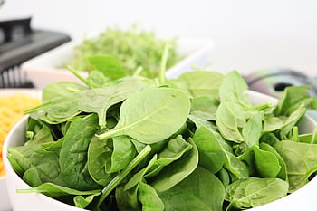 A close-up of fresh spinach leaves in a white bowl, ideal for healthy salads. HD wallpaper