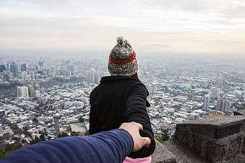 A couple holding hands overlooking a vast urban cityscape, emphasizing travel and togetherness. HD wallpaper
