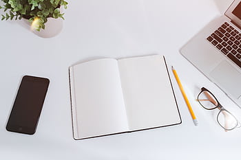 An organized workspace with a notebook, smart, and laptop on a bright, clean desk. HD wallpaper