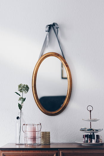 A stylish interior setup featuring a hanging oval mirror with decorative elements on a wooden table. HD phone wallpaper