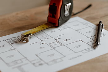 Close-up view of architectural blueprint with measuring tape and pen on a wooden table. HD wallpaper