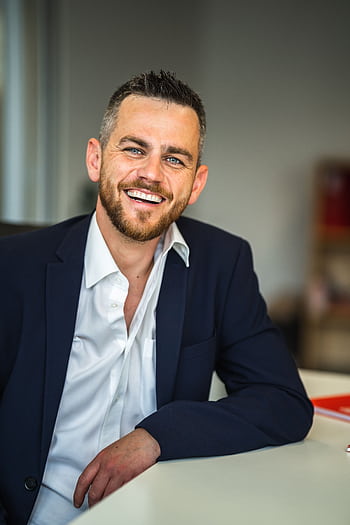 Business professional in suit smiling confidently in a modern office environment. HD phone wallpaper