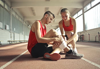 A woman helps an injured man's leg on an indoor track, providing first aid. HD wallpaper