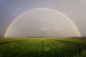 A full rainbow arches over a serene farmland landscape, capturing natural beauty. HD wallpaper