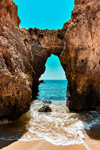 Capture of a natural rock arch framing a stunning ocean view on a sunny day. HD phone wallpaper