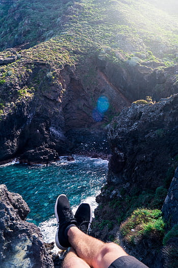 Person relaxing on a cliff overlooking the ocean, capturing adventure in nature. HD phone wallpaper