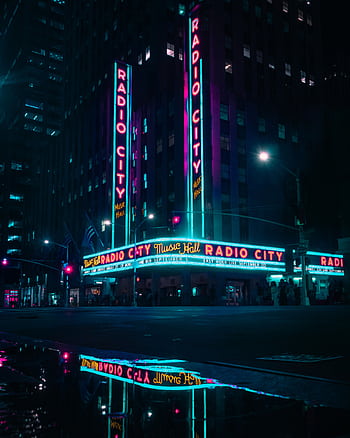 Vibrant nighttime view of Radio City Music Hall with neon lights and reflections. HD phone wallpaper