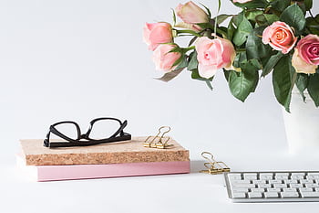 Stylish workspace featuring pink roses, glasses, keyboard, and notebooks. Perfect for spring office decor. HD wallpaper