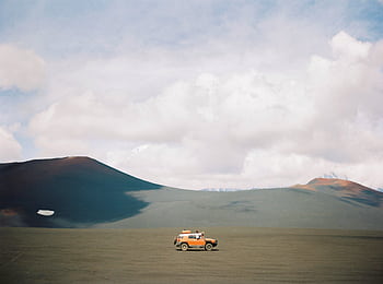 A lone SUV exploring the remote landscapes of Kamchatka under a vast, cloudy sky. HD wallpaper