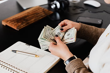 Person counting cash with a planner and gold pen on a desk, representing financial management. HD wallpaper