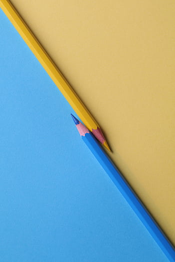 Close-up of vibrant yellow and blue colored pencils on contrasting paper backgrounds. HD phone wallpaper