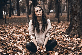 A woman sits thoughtfully on fallen leaves in a park, capturing an autumnal mood. HD wallpaper