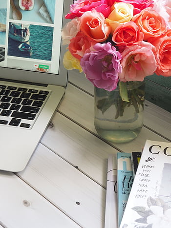 Bright and modern home office setup with a laptop, magazines, and a vibrant floral arrangement in a vase. HD phone wallpaper