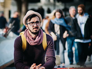 A stylish man in a trendy outfit stands out on a busy city street with various people in the background. HD wallpaper