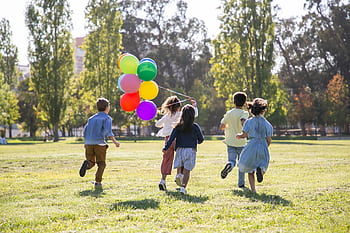 Children happily running with balloons in a sunny park, capturing friendship and joy. HD wallpaper
