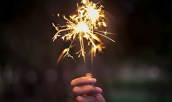A hand holding sparklers glowing brightly in a dark night, capturing the essence of celebration. HD wallpaper