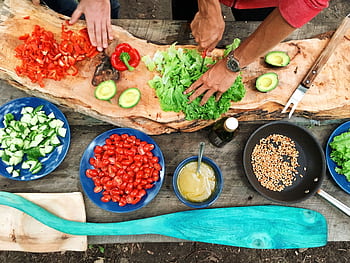 Fresh ingredients being prepared on a rustic wooden table, showcasing vibrant vegetables and hands at work. HD wallpaper