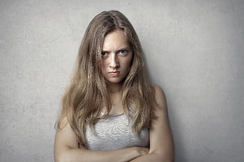 Portrait of a fierce woman with crossed arms and intense expression on a gray background. HD wallpaper
