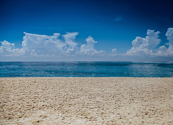 A tranquil beach scene with clear skies and gentle ocean waves, perfect for relaxation. HD wallpaper