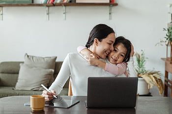 A loving mother and daughter embrace while working remotely from home with a laptop. HD wallpaper