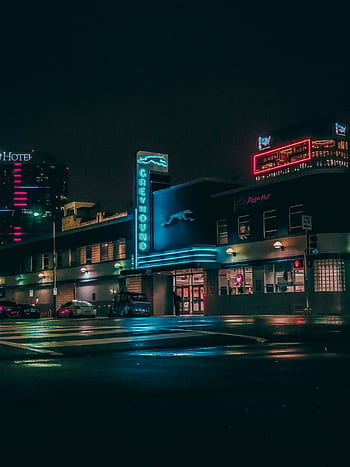 Vibrant nighttime scene of a Greyhound bus station with neon signs in an urban setting. HD phone wallpaper