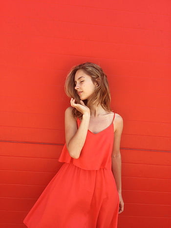 Portrait of a young woman wearing a stylish red dress, posing gracefully against a matching red background. HD phone wallpaper