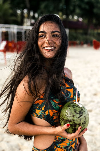 A cheerful woman at the beach holding a coconut, exuding happiness and summer vibes. HD phone wallpaper