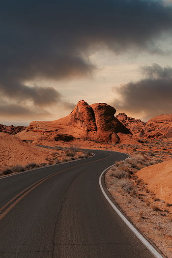 Scenic winding road in desert with red rock formations and dramatic clouds, NV, USA. HD phone wallpaper