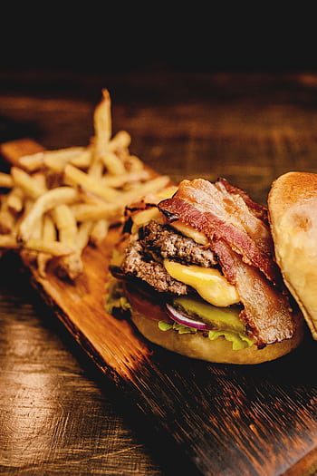 Savor a mouthwatering bacon cheeseburger with crispy fries on a rustic wooden board. Perfect fast food indulgence. HD phone wallpaper