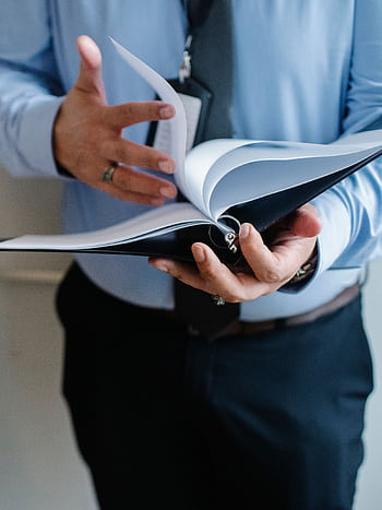 A business professional in a suit flips through documents indoors, emphasizing formal work settings. HD phone wallpaper